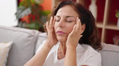 Orta yaşlı İspanyol kadın baş ağrısı çekiyor. Evdeki koltukta oturuyor.