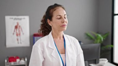 Klinikte steteskop takarak gülümseyen orta yaşlı İspanyol kadın doktor