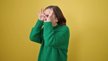 Gri saçlı olgun İspanyol kadın. Gözlük takıyor. Elleri izole edilmiş sarı arka planda.