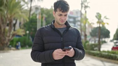 Genç İspanyol adam akıllı telefon kullanarak parka bakıyor.