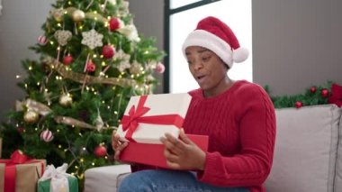 Afrika kökenli Amerikalı bir kadın Noel şapkası takıyor ve evinde şaşırmış bir yüz ifadesi var.