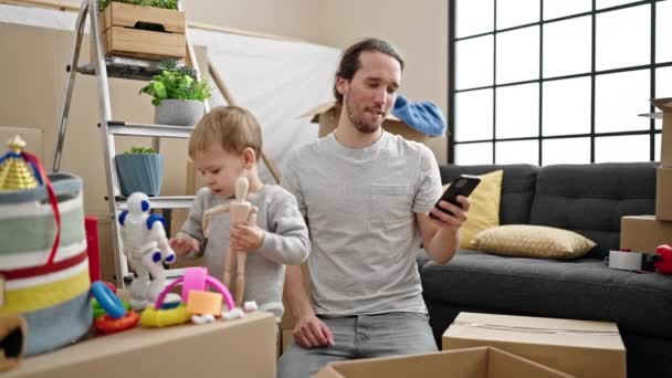 Pai Filho Desempacotando Caixa Papelão Usando Smartphone Nova Casa — Vídeo de Stock