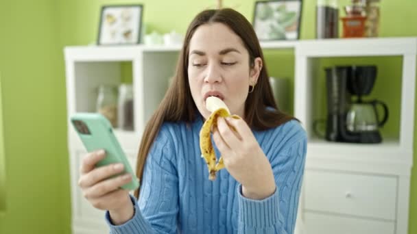 Młoda Kaukaska Kobieta Jedzenie Banan Pomocą Smartfona Jadalnia — Wideo stockowe