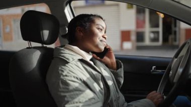 Afro-Amerikalı kadın akıllı telefondan konuşuyor. Sokakta arabada oturuyor.