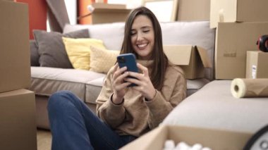 Güzel İspanyol kadın akıllı telefon kullanıyor. Yeni evinde yerde oturuyor.