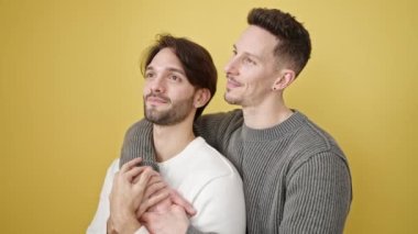 Birbirlerine sarılan iki erkek izole edilmiş sarı arka planda duruyor.