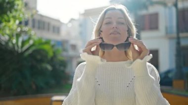 Parkta güneş gözlüğü takan, kendine güvenen genç sarışın kadın.