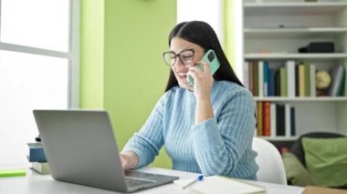 Genç İspanyol öğrenci kütüphanedeki telefonda dizüstü bilgisayar kullanıyor.