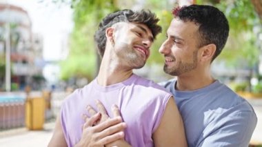 Two men couple smiling confident hugging each other at park