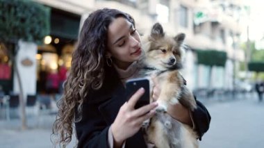 Köpeğiyle gülümseyen genç İspanyol kadın. Sokakta akıllı telefon kullanıyor.