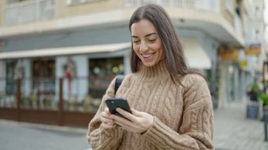 Genç ve güzel İspanyol kadın sokakta akıllı telefon dansı yapıyor.