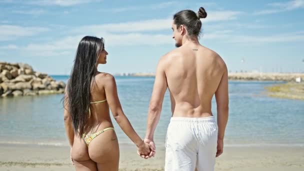 男と女の観光客カップルは ビーチで一緒に手で歩いています — ストック動画