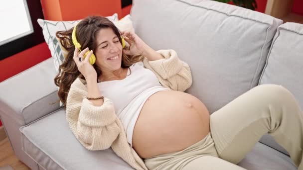 Молодая Беременная Женщина Слушает Музыку Надевая Наушники Живот Дома — стоковое видео