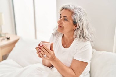 Orta yaşlı kadın yatakta kahve içiyor.