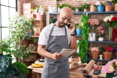 Genç, kel bir çiçekçi çiçekçide akıllı telefondan not defteri okuyor.