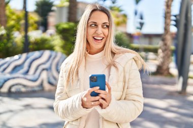 Parkta akıllı telefon kullanan kendine güvenen genç bir kadın.