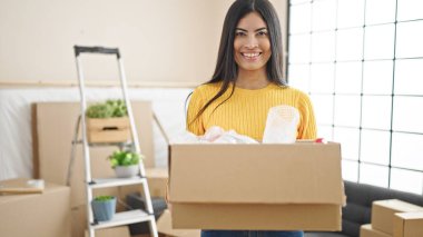 Young beautiful hispanic woman smiling confident holding package at new home