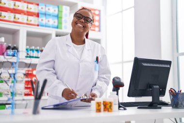 African american woman pharmacist writing on checklist at pharmacy