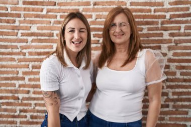 Hispanic mother and daughter wearing casual white t shirt winking looking at the camera with sexy expression, cheerful and happy face. 