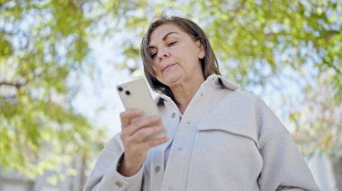 Orta yaşlı İspanyol kadın parkta akıllı telefon kullanıyor.