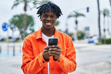 Sokakta akıllı telefon kullanan, kendinden emin gülümseyen Afrikalı Amerikalı bir adam.