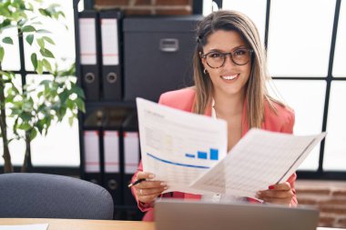 Young hispanic woman business worker using laptop reading document at office