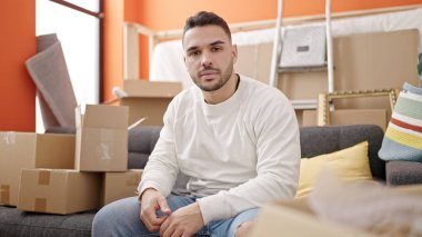 Yeni evinde ciddi bir ifadeyle koltukta oturan İspanyol asıllı genç adam.