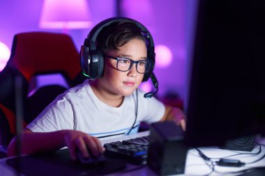 Adorable hispanic boy streamer playing video game using computer at gaming room
