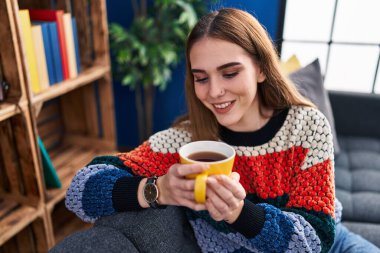 Young woman drinking coffee sitting on sofa at home