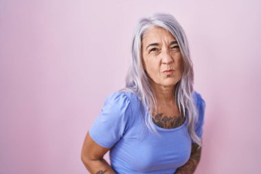 Orta yaşlı bir kadın, elleri karnında pembe arka planda duran dövmeleri var. Çünkü hazımsızlık, acı verici bir hastalık, kendini iyi hissetmiyor. Ağrı kavramı. 