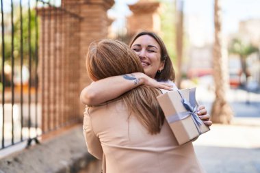 Mother and daughter hugging each other surprise with gift at street