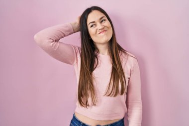 Young brunette woman standing over pink background confuse and wondering about question. uncertain with doubt, thinking with hand on head. pensive concept. 