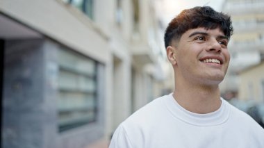 Young hispanic man smiling confident looking to the side at street