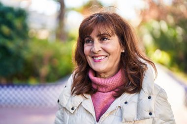 Orta yaşlı bir kadın parkta kendine güvenerek gülümsüyor.