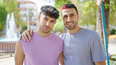 Two men couple smiling confident hugging each other at park