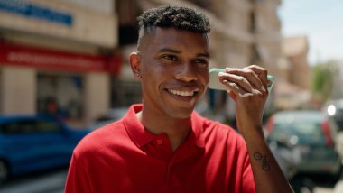 Genç Latin adam gülümsüyor. Caddedeki akıllı telefondan kendine güvenen bir sesli mesaj dinliyor.