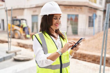Young beautiful hispanic woman architect smiling confident using smartphone at street