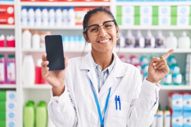 Eczanede çalışan Latin kökenli genç bir kadın akıllı telefon ekranında gülümsüyor. 