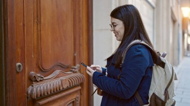 Sırt çantalı genç İspanyol kadın turist akıllı telefon kullanarak caddede adres arıyor.