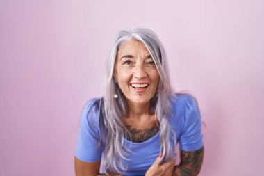 Pembe arka planda dövmeleri olan orta yaşlı bir kadın gülümseyerek ve kahkahalarla gülüyor.. 