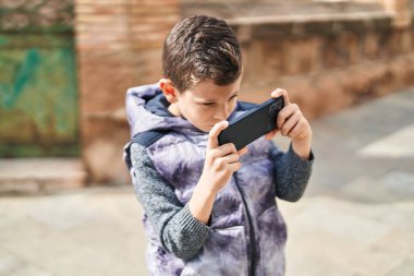 Blond child playing video game by the smartphone at street