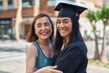 Two women mother and graduated daughter hugging each other at street