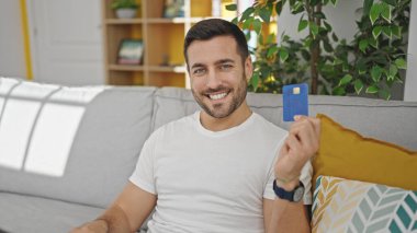 Evdeki kanepede oturan, elinde kredi kartı olan genç bir İspanyol.