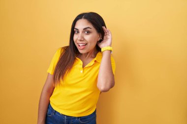 Sarı arka planda dikilen genç Arap kadın kulağına fısıldayarak dedikoduları ve dedikoduları dinliyor. Sağırlık kavramı. 