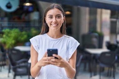 Kahve dükkanının terasında akıllı telefon kullanan, kendine güvenen, güzel İspanyol bir kadın.