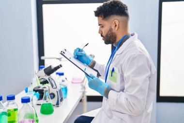 Bilim adamı üniforması giyen genç İspanyol adam laboratuardaki panoya yazı yazıyor.