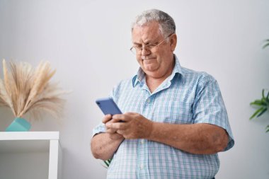 Middle age grey-haired man using smartphone standing at home