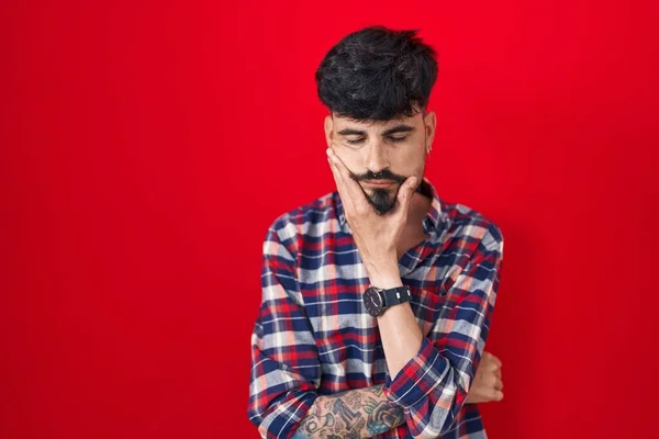Joven Hombre Hispano Con Barba Pie Sobre Fondo Rojo Pensando — Foto de Stock
