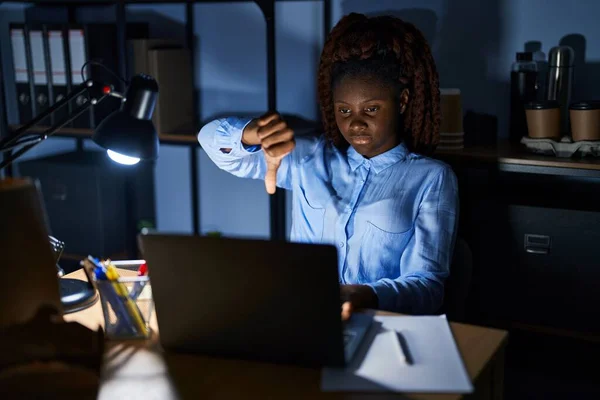 African woman working at the office at night looking unhappy and angry showing rejection and negative with thumbs down gesture. bad expression.