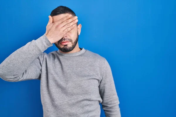 Hispanic Man Standing Blue Background Covering Eyes Hand Looking Serious — Foto de Stock